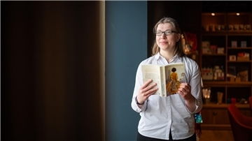 Eine Frau mit weißer Bluse trägt hält ein Buch in der Hand.
