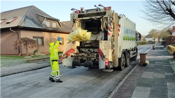 Ein Mann wirft einen gelben Sack in das Fahrzeug der Müllabfuhr.
