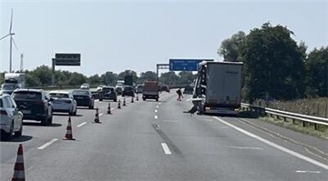 Auf einer dreispurigen Straße steht rechts ein LKW. Die linke Spur ist abgesperrt und dort fahren hintereinander mehrere Autos.