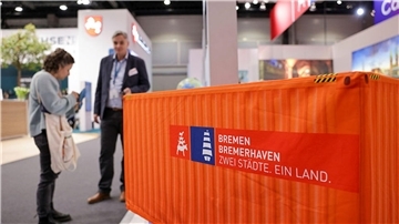 Ein Mann und eine Frau stehen neben einem Mini-Container an einem Messestand.