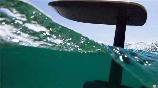 Unter dem Surfboard ragt ein Mast ins Wasser. An ihm sind zwei Tragflächen angebracht, die wie die Flügel eines Flugzeugs Auftrieb geben.
