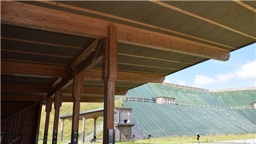 Unter Holzdächern ist das Dämmmaterial bereits angebracht, im Hintergrund ist der Lärmschutzwall zu sehen.
