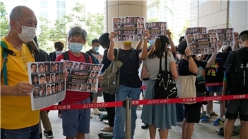 Unterstützer halten vor einem Gericht in Hongkong Plakate mit den Fotos einiger der 47 angeklagten Demokratie-Aktivisten in die Höhe.