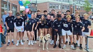 Viele Jungen und Mädchen stehen in Sportkleidung nebeneinander und davor steht ein Hund.