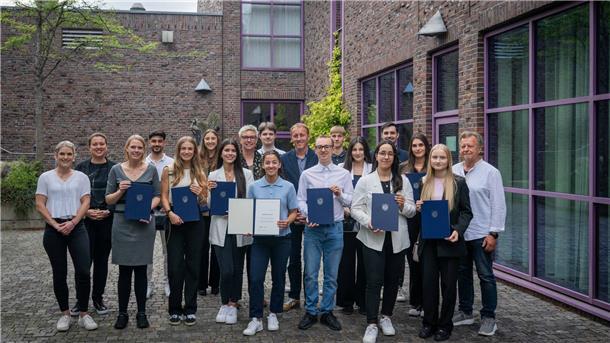 Gruppenfoto von vielen Menschen vor einem Gebäude. Einige halten Urkunden und blaue Mappen in den Händen. Stadtrat Hauke Hilz überreichte im Historischen Museum Bremerhaven 15 Lehramtsstudierenden feierlich die Stipendienurkunden.
