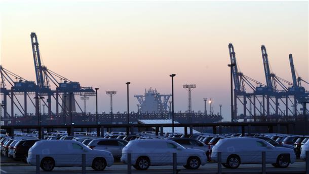 Hafenkulisse mit Autos im Vordergrund und Containerbrücken im Hintergrund.