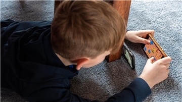 Ein Junge liegt auf dem Fußboden und spielt ein Spiel an seinem Handy. Glücksspiel im Gaming: Niedersachsen fordert strengere Regeln für bestimmte Videospiele.