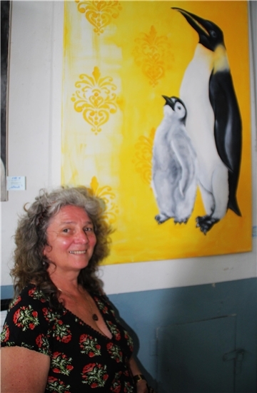 Eine Frau steht vor einem Bild. Abgebildet sind dort auf gelbem Hintergrund zwei Pinguine.