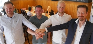 Vier Männer stehen nebeneinander und legen je eine Hand auf die Hände der anderen.