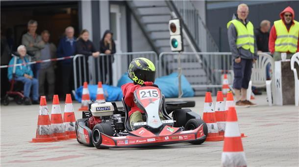 Ein Kartfahrer fährt auf einer Strecke zwischen Pylonen. Im Hintergrund sind Helfer in Warnweste und einige Zuschauer zu sehen.