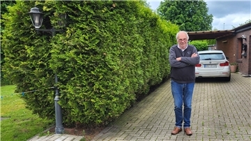 Ein Mann steht mit verschränkten Armen auf seiner Hauseinfahrt. 