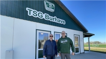 Zwei Männer stehen vor einem Gebäude mit der Aufschrift TSG Burhave. Günter Thielemann und Volker Bliefernich sind voller Stolz auf den Neubau.