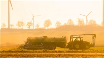 Mit einem Traktor wird bei Sonnenaufgang ein Feld mit Gülle gedüngt