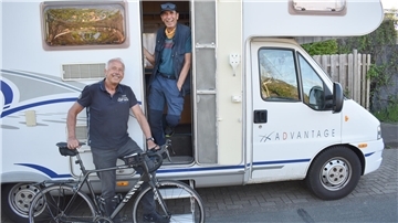 Zwei Männer, einer mit einem Fahrrad, stehen an einem Wohnmobil.