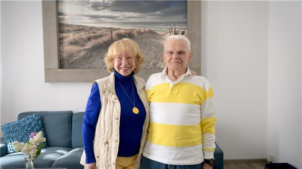 Eine Frau und ein Mann stehen in einem Wohnzimmer vor einem Bild, welches Strand und Meer zeigt.