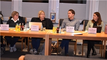 Drei Frauen und ein Mann sitzen an einer Tischreihe.
