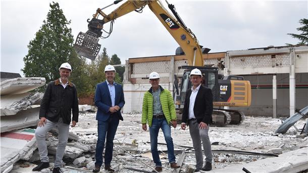 Vier Männer mit Bauhelmen stehen in einer Baustelle vor einem Kran.