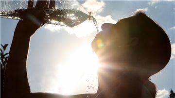 Eine Person trinkt aus einer Wasserflasche bei strahlender Sonne.