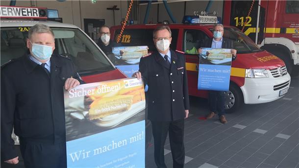 Geestland will als Modellkommune öffnen Wenn Geestland Modellkommune wird, könnten diese Plakate bald in den Geschäften und Restaurants hängen – und die örtlichen Feuerwehrhallen zu Testzentren werden. Darauf hoffen (von links): Matthias Witte, Bürgermeister Thorsten Krüger, Friedrich Meyerherm und Henning Dageförde.