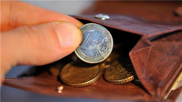 Eine Hand nimmt eine Ein-Euro-Münze aus einer braunen Brieftasche und hält sie in die Kamera.