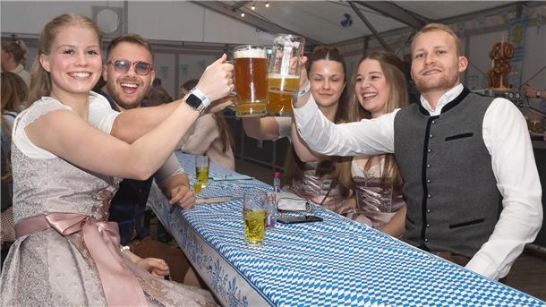 Junge Leute in Bayerntrachten und Dirndl prosten sich bei der Party in Abbehausen mit Bierkrügen zu. 