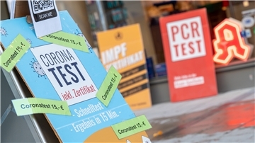 Schilder mit der Aufschrift „Corona Test - inkl. Zertifikat - Coronatest 15,- Euro“, „Impfzertifikat“ und „PCR -Test“ stehen vor einer Apotheke in der Innenstadt
