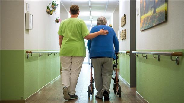 Eine Pflegekraft hilft einem Patienten, der auf den Rollator angewiesen ist, bei der Fortbewegung.