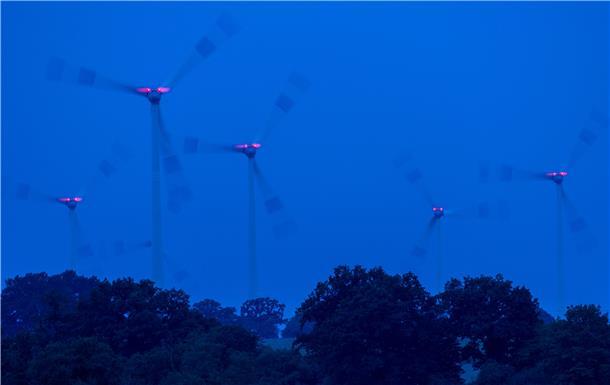 Windräder drehen sich vor Sonnenaufgang und werden von roten Warnleuchten markiert.