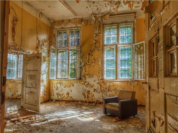 Wie Herbstlaub blättern die Tapeten von den Wänden dieses Raumes eines historischen Gebäudes. Ein verlorener Sessel zeugt davon, dass das Zimmer einst bessere Zeiten kannte.