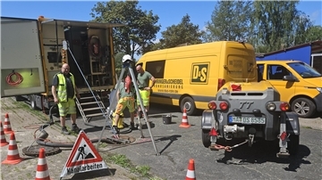 Kanalarbeiten in einer Straße mit Fahrzeugen, Maschinen und Arbeitern.