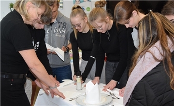 Wie sich Servietten für die Gastronomie dekorativ falten lassen, zeigt Serviceleitung Martina Stelljes (links)  vom Ringhotel Paulsen den Oberschülern und lässt diese ebenfalls Hand anlegen.