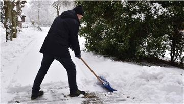 Schneeräumpflicht - Was Sie beachten müssen Ein Mann schaufelt Schnee mit einem Schneeschieber.