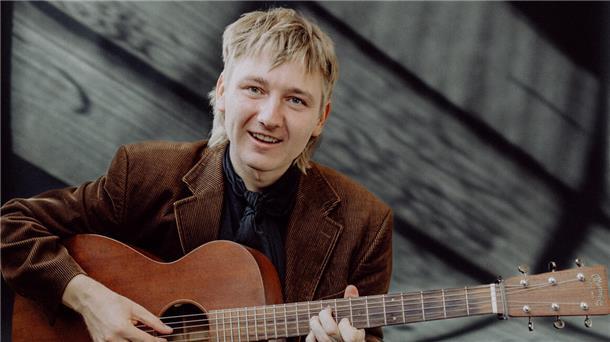 Konzert in der Mühle - Der Vorverkauf für beliebten Künstler läuft Ein junger Mann lächelt in die Kamera und zupft an seiner Gitarre.