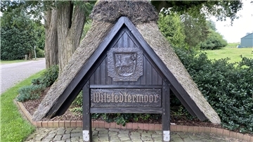 Ein Holzschild mit Strohdach und der Aufschrift Wilstedtermoor. 