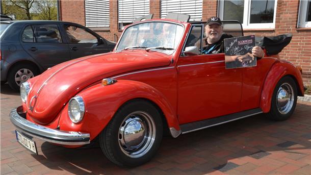 Wolfgang Dziony, Gründungsmitglied der Scorpions, im feuerroten VW-Cabrio. Er zeigt das erste Studioalbum der Scorpions, an dem er mitgewirkt hat, Lonesome Crow. Neben ihm im Auto: der Kulturjournalist Ralf G. Poppe aus Bremervörde.