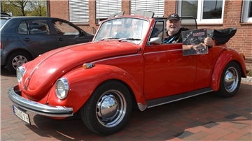 Wolfgang Dziony, Gründungsmitglied der Scorpions, im feuerroten VW-Cabrio. Er zeigt das erste Studioalbum der Scorpions, an dem er mitgewirkt hat, Lonesome Crow. Neben ihm im Auto: der Kulturjournalist Ralf G. Poppe aus Bremervörde.