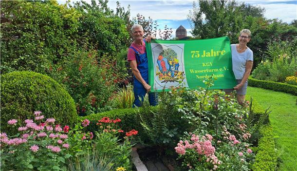 Vom Grabeland zur Gartenidylle: 75 Jahre Kleingartenverein Wasserturm Bild von Wolfgang Engels, Vorsitzender des Kleingartenvereins Wasserturm in Nordenham, und seiner Frau Jutta mit einem Banner zum 75-jährigen Bestehen des Vereins.