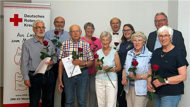 Gruppe von zehn Personen, die beim DRK geehrt wurden, stehen mit roten Rosen und Urkunden in der Hand vor einem Banner des Deutschen Roten Kreuzes.
