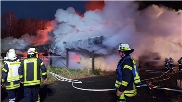 Drei Feuerwehrmänner vor einem brennenden Gebäude.