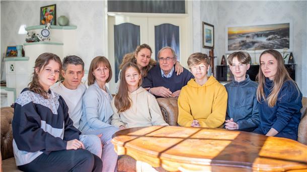 Die Familien sitzen gemeinsam an einem Tisch und blicken in die Kamera.
