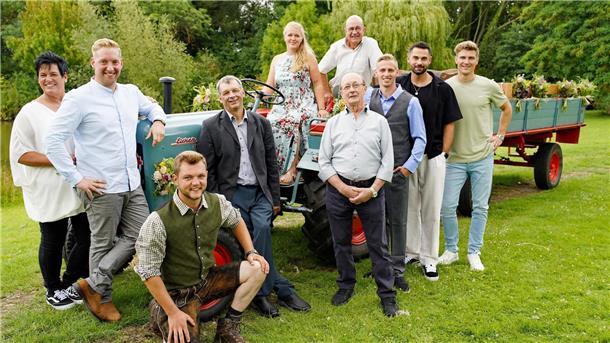 Menschen stehen um einen Traktor im Freien herum, zwei sitzen drauf.