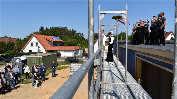 Zeremonie in schwindelnder Höhe: Holger Schmidt, Geschäftsführer der für den Holzrahmenbau verantwortlichen Debstedter Firma, spricht den Richspruch, sein Team hebt - wie es im Zimmererhandwerk alte Sitte ist - den einen oder anderen „Kurzen“, und die Gäste hören zu.