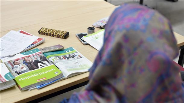 Eine Frau mit Kopftuch sitzt an einem Tisch, auf dem Lernmaterial liegt.