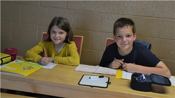 Eine Schülerin und ein Schüler sitzen an ihren Heften.