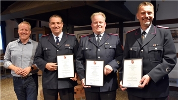 Drei Feuerwehrleute stehen neben einem Mann und halten eine Urkunde in den Händen.