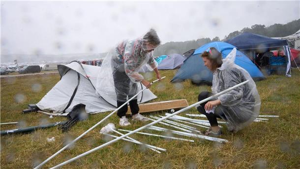 Zwei Fans bauen auf dem Campinggelände des Technofestivals „Nature One“ bei strömendem Regen ihr Zelt auf.
