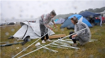 Zwei Fans bauen auf dem Campinggelände des Technofestivals „Nature One“ bei strömendem Regen ihr Zelt auf.