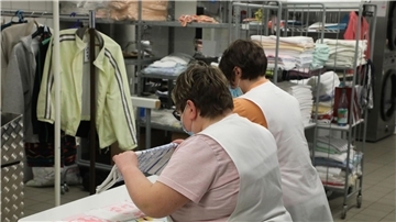 Zwei Frauen arbeiten in der Wäscherei der Lebenshilfe Gera e.V und legen dort Wäsche zusammen.