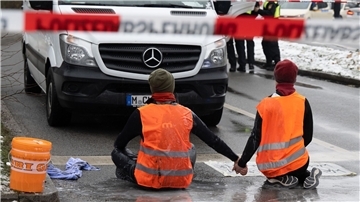 Zwei Klimaaktivisten der „Letzten Generation“ versuchen, sich auf einer Straße in München trotz Nieselregen und Minusgraden festzukleben.