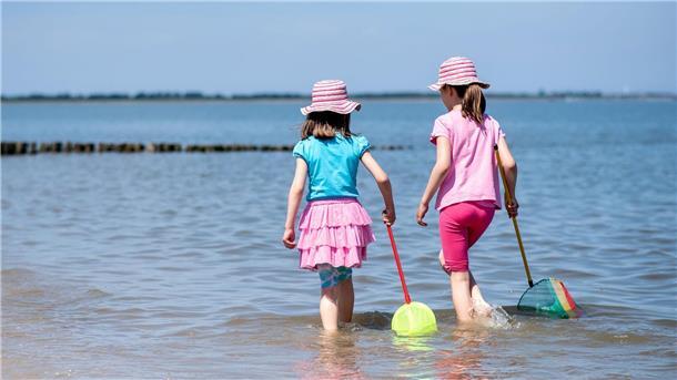 Zwei Mädchen spielen bei sonnigem Wetter mit ihren Keschern im flachen Wasser der Nordsee am Strand.